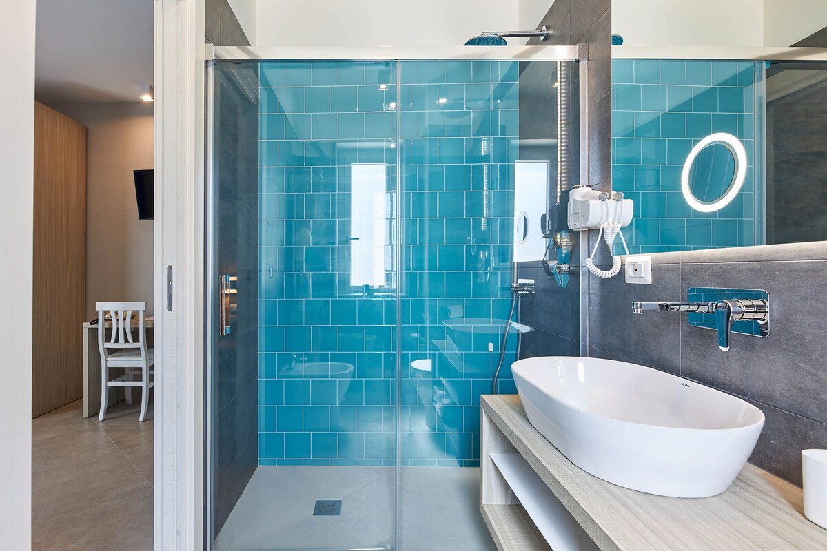 A modern bathroom with a glass shower enclosure, a white sink, and a towel rack.