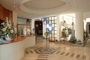 A hotel reception area with a wooden reception desk, a large floral arrangement, and a staircase leading to another floor. - La Sorgente (Capaccio-Paestum)