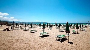 A beach with rows of sun loungers and umbrellas, a clear sky, and a distant view of the sea and mountains. - La Sorgente (Capaccio-Paestum)
