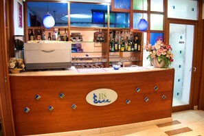 A hotel reception area with a wooden counter, a coffee machine, and a variety of bottles and glasses on shelves. - La Sorgente (Capaccio-Paestum)