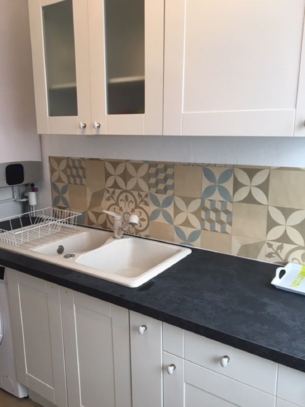 A kitchen with a double sink, white cabinets, a black countertop, and patterned backsplash tiles.