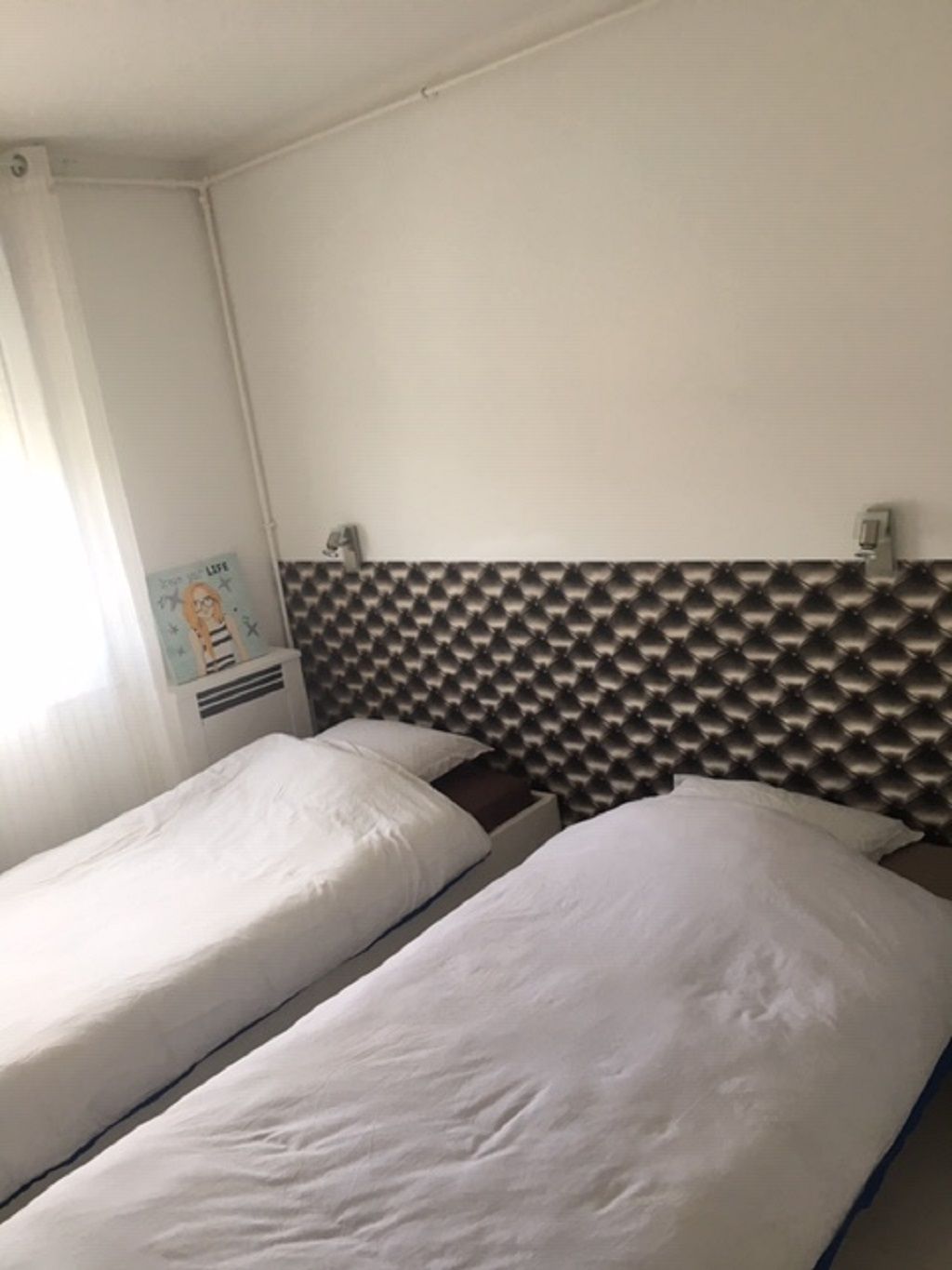 Une chambre avec deux lits simples, une tête de lit blanche et une affiche accrochée au mur.