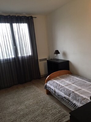 A bedroom with a bed, a nightstand, a lamp, and a window with curtains.