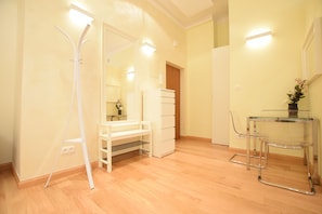 A hotel room with a wooden floor, a white wardrobe, a glass table with chairs, and a mirror.