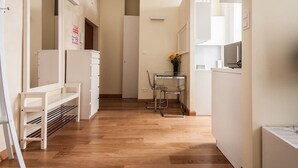 Un pasillo con un banco blanco, una pequeña mesa con sillas y una puerta con un letrero de 'No Smoking'.