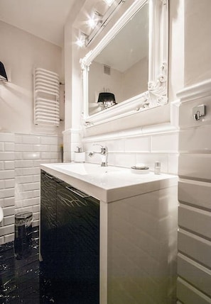 A bathroom with a white sink, a mirror with a decorative frame, and a black tiled floor.