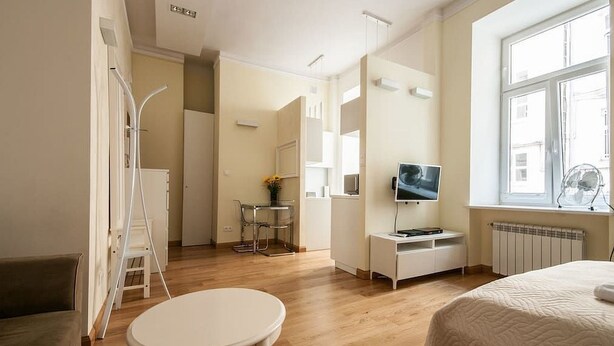 Habitación de hotel moderna con cama, una pequeña mesa redonda, televisor y una zona de kitchenette.