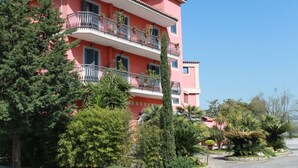 A multi-story pink building with balconies, surrounded by various trees and shrubs. - Hotel Tiro a Volo (Pozzuoli)