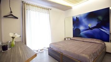 A bedroom with a bed, a bedside table, a hanging light, a window with curtains, and a painting on the wall.