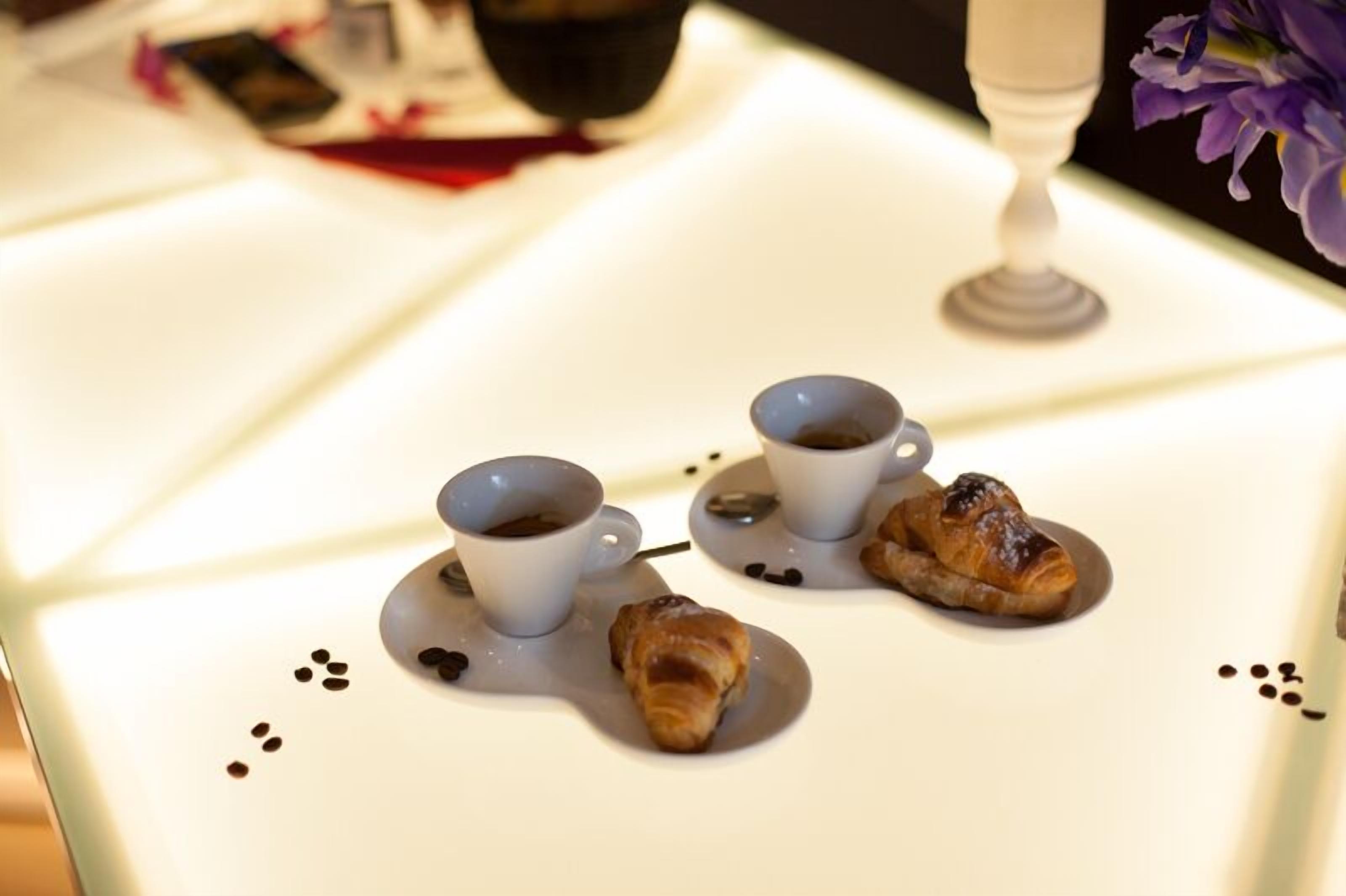 A table with two cups of coffee and two pastries, possibly croissants, with coffee stains on the table.