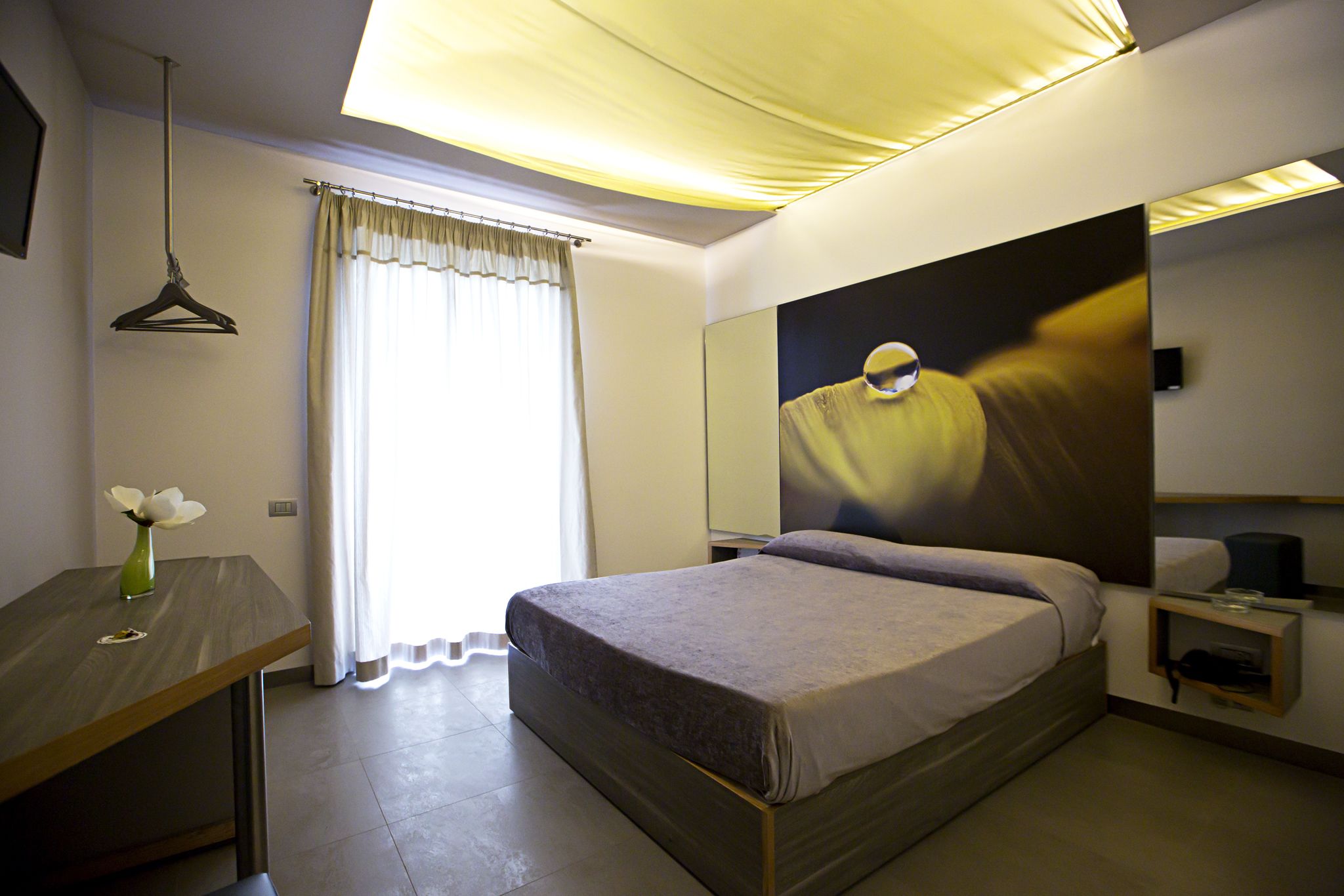 Habitació d'hotel moderna amb llit, taula de nit i un quadre gran a la paret.