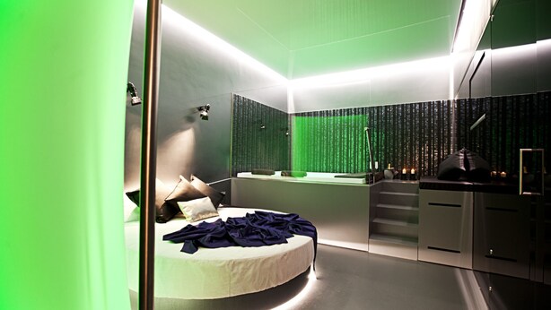 A modern bedroom with a curved bed, a small desk, and a green-lit wall. - Hotel Tiro a Volo (Pozzuoli)