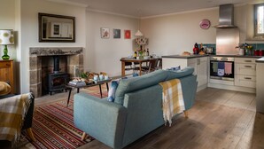 A cozy living room with a sofa, a fireplace, a dining table with chairs, and a kitchen area with modern appliances. - A beautiful and cosy dog friendly cottage with flexible sleeping arrangements (Greenlaw)