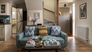 A living room with a sofa, a coffee table with books and pastries, a vase with flowers, and a staircase in the background. - A beautiful and cosy dog friendly cottage with flexible sleeping arrangements (Greenlaw)