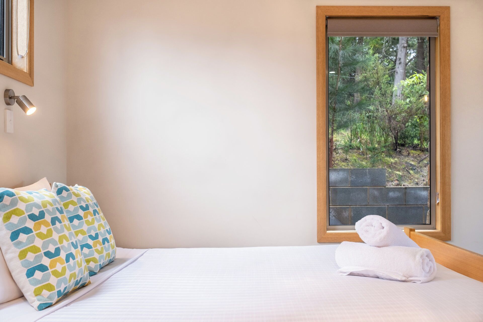 Une chambre à coucher avec un lit, des coussins à motifs, une fenêtre donnant sur un paysage verdoyant et une serviette sur le lit.