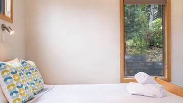 Une chambre à coucher avec un lit, des coussins à motifs, une fenêtre donnant sur un paysage verdoyant et une serviette sur le lit.