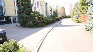 A pathway leading to a multi-story building with a mix of red, white, and yellow facades, surrounded by greenery and trees.