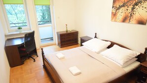 A bedroom with a wooden bed, a desk, a chair, a dresser, and a window with a view of trees.