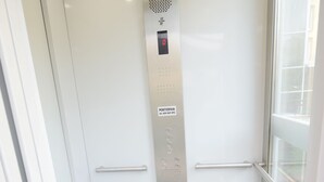 A narrow elevator with metallic doors and a control panel.