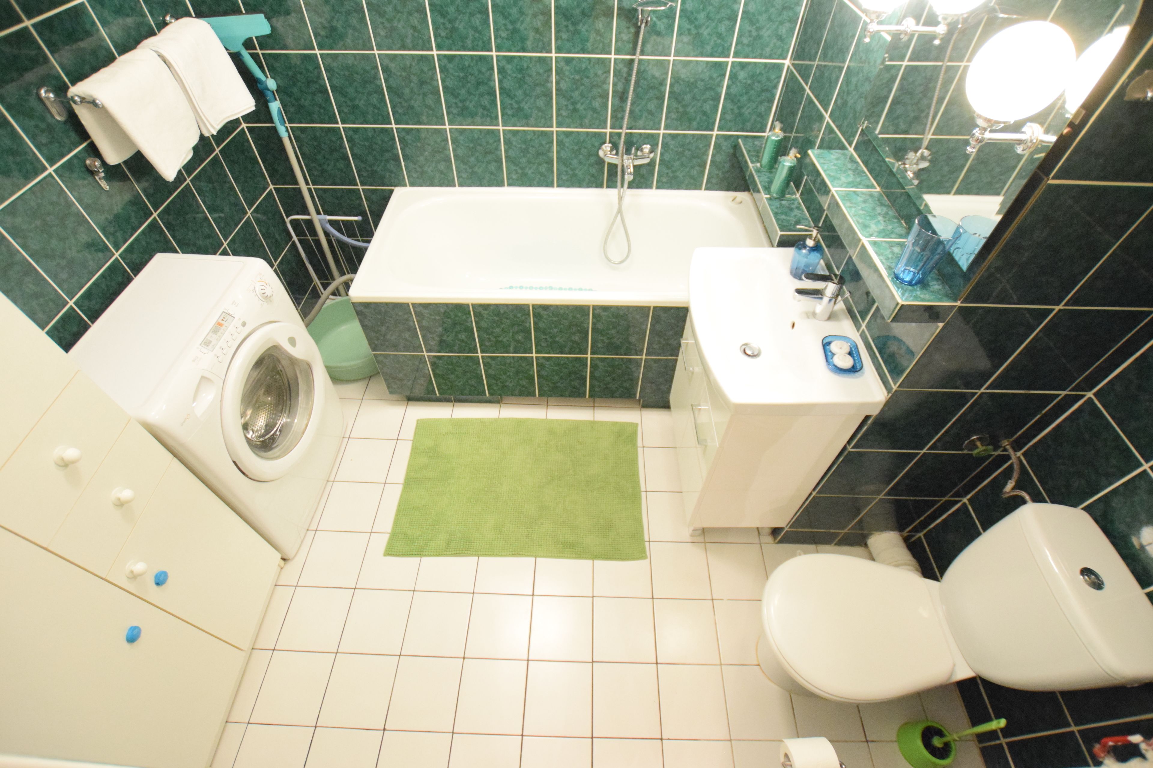 Ein Badezimmer mit Waschmaschine, Badewanne, Toilette und einem grünen Teppich.