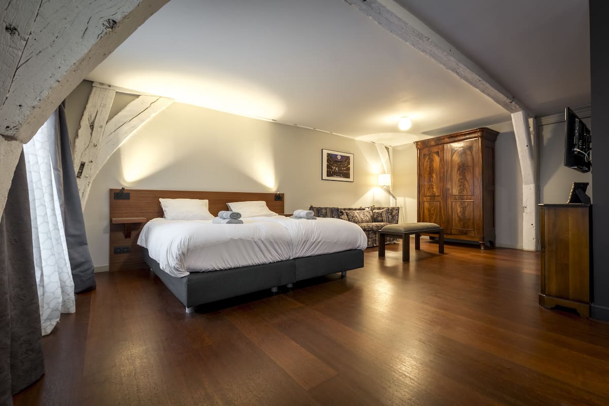 A bedroom with a large bed, wooden floor, a wooden wardrobe, and a bench.
