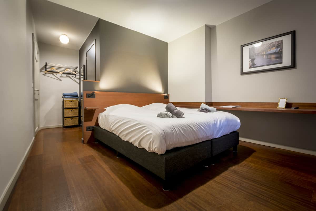 A modern bedroom with a dark wooden bed, a bedside table, a hanging light fixture, and a framed picture on the wall.