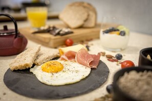 Une assiette de petit-déjeuner avec un œuf, du jambon, du fromage et du pain, le tout servi sur une ardoise.