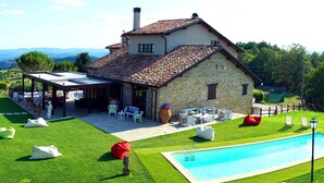 Ein Haus aus Stein mit Ziegeldach, einem Schwimmbecken und einer Terrasse mit Gartenmöbeln.