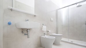 Un baño moderno con lavamanos, inodoro y bidé blancos, zona de ducha y espejo.