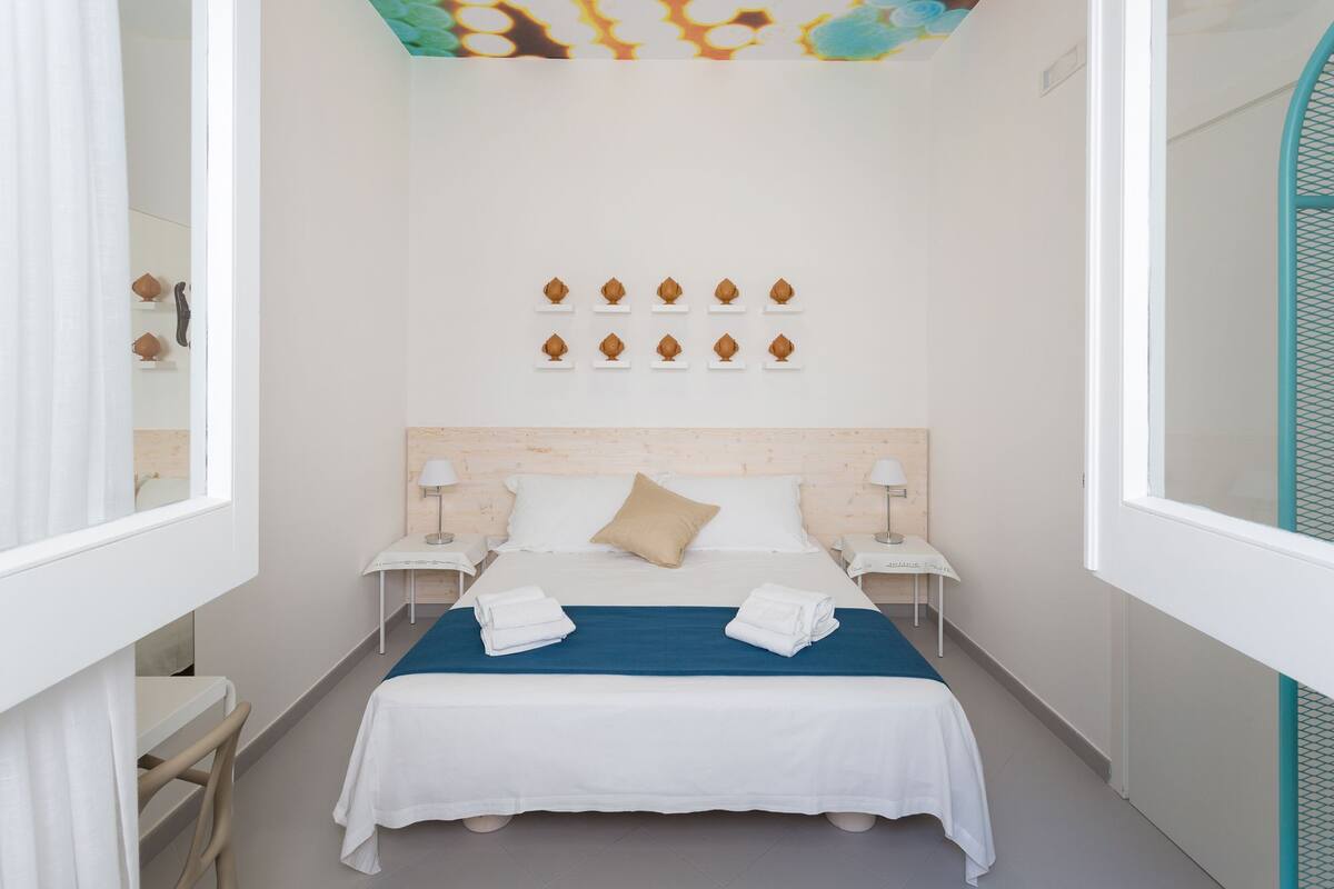 Una habitación de hotel con cama, dos mesitas de noche, una lámpara de pared y un adorno mural.