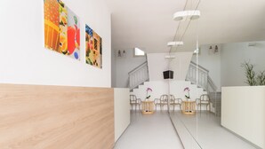 Una moderna zona de recepción con un mostrador de madera, dos mesas redondas con sillas y una escalera.