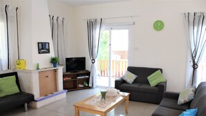 A living room with a sofa, a coffee table, a TV, and a sliding glass door leading to a balcony. - Vasilisa villa BW16 (Paralimni)