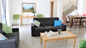 A living room with a sofa, a coffee table, and a dining area with chairs and a table. - Vasilisa villa BW16 (Paralimni)