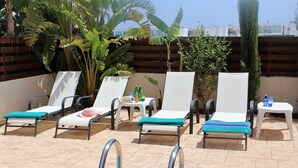 A poolside area with lounge chairs, a small table with drinks, and a wooden fence. - Vasilisa villa BW16 (Paralimni)