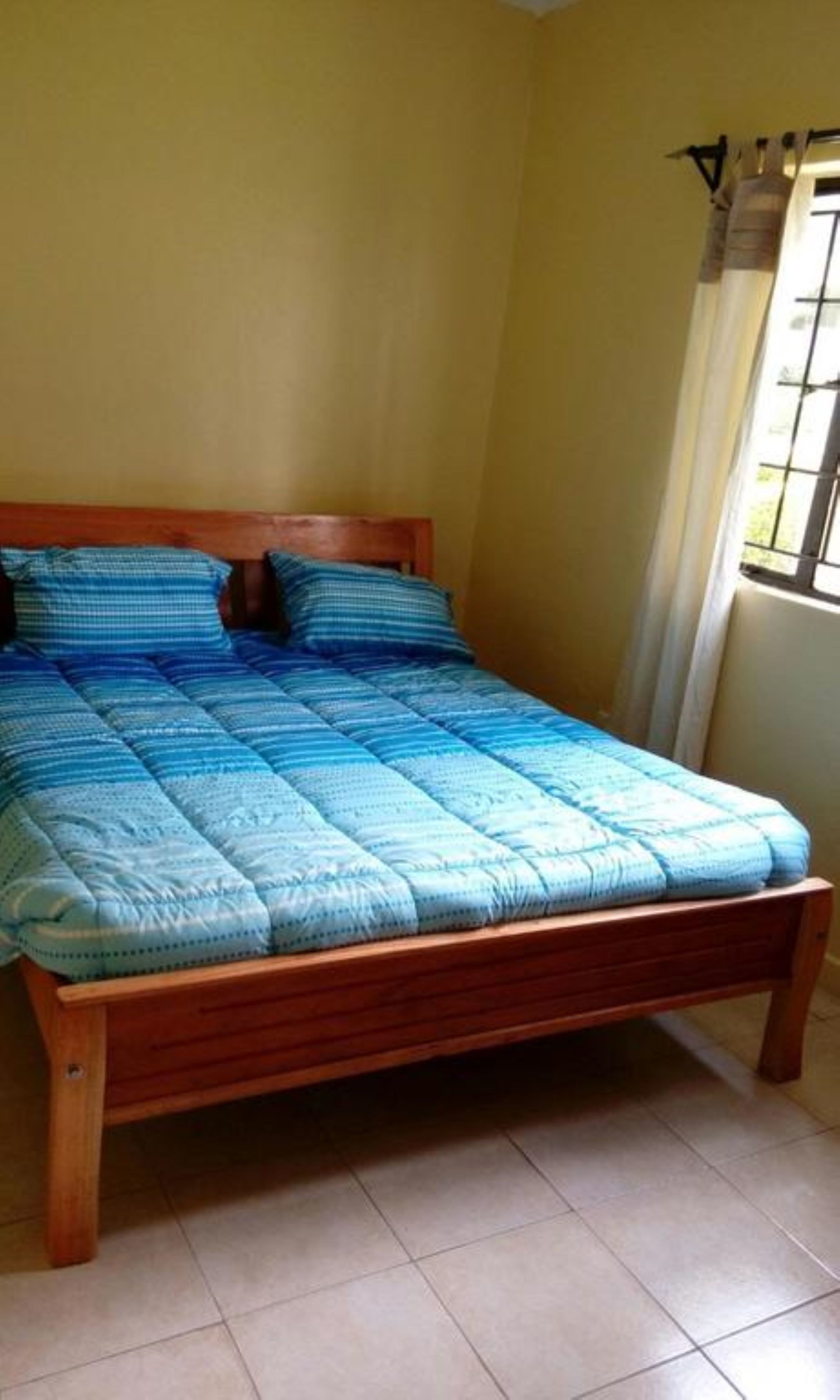 A bed with a blue quilt in a room with yellow walls and a window with bars.