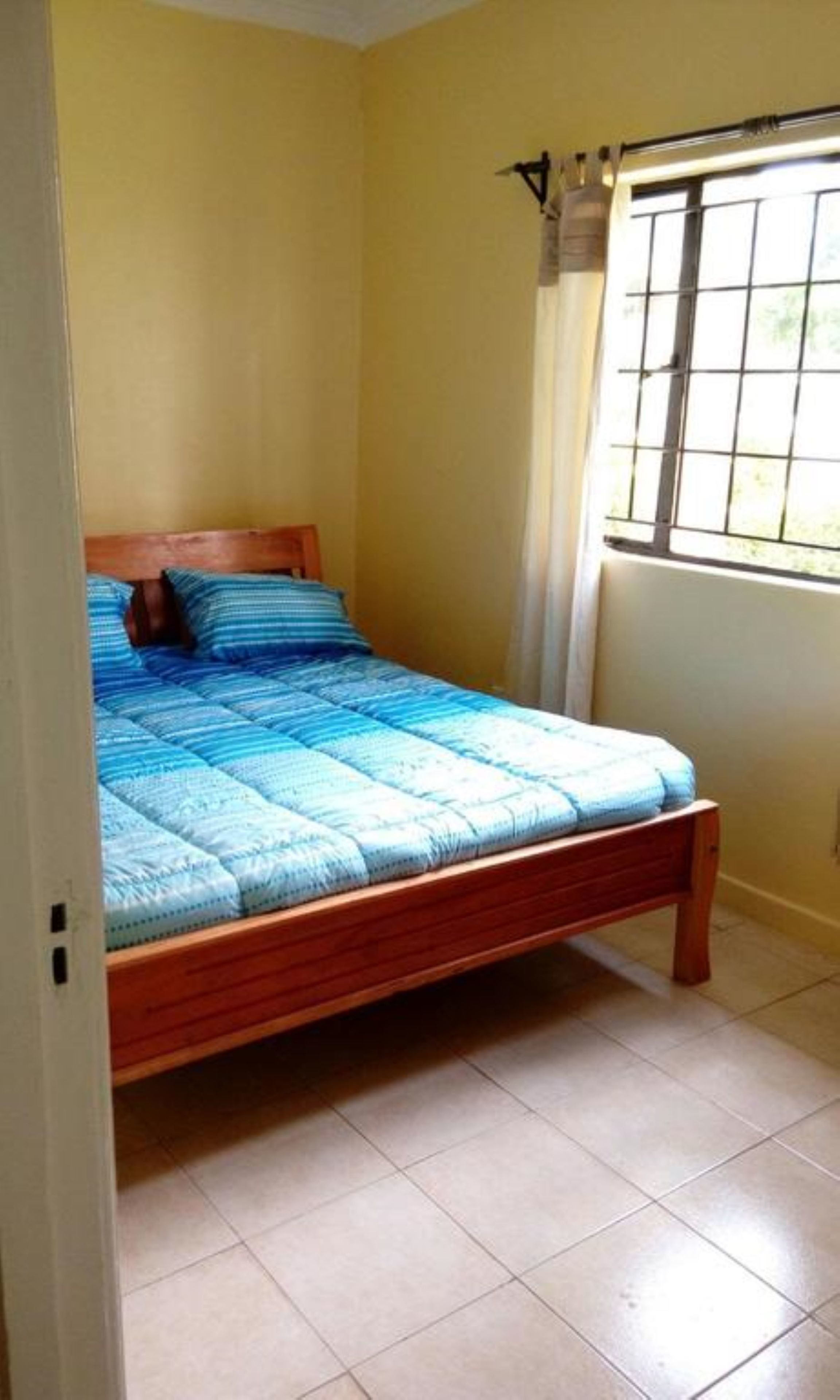 A single bed in a room with yellow walls and a window with a metal grid.