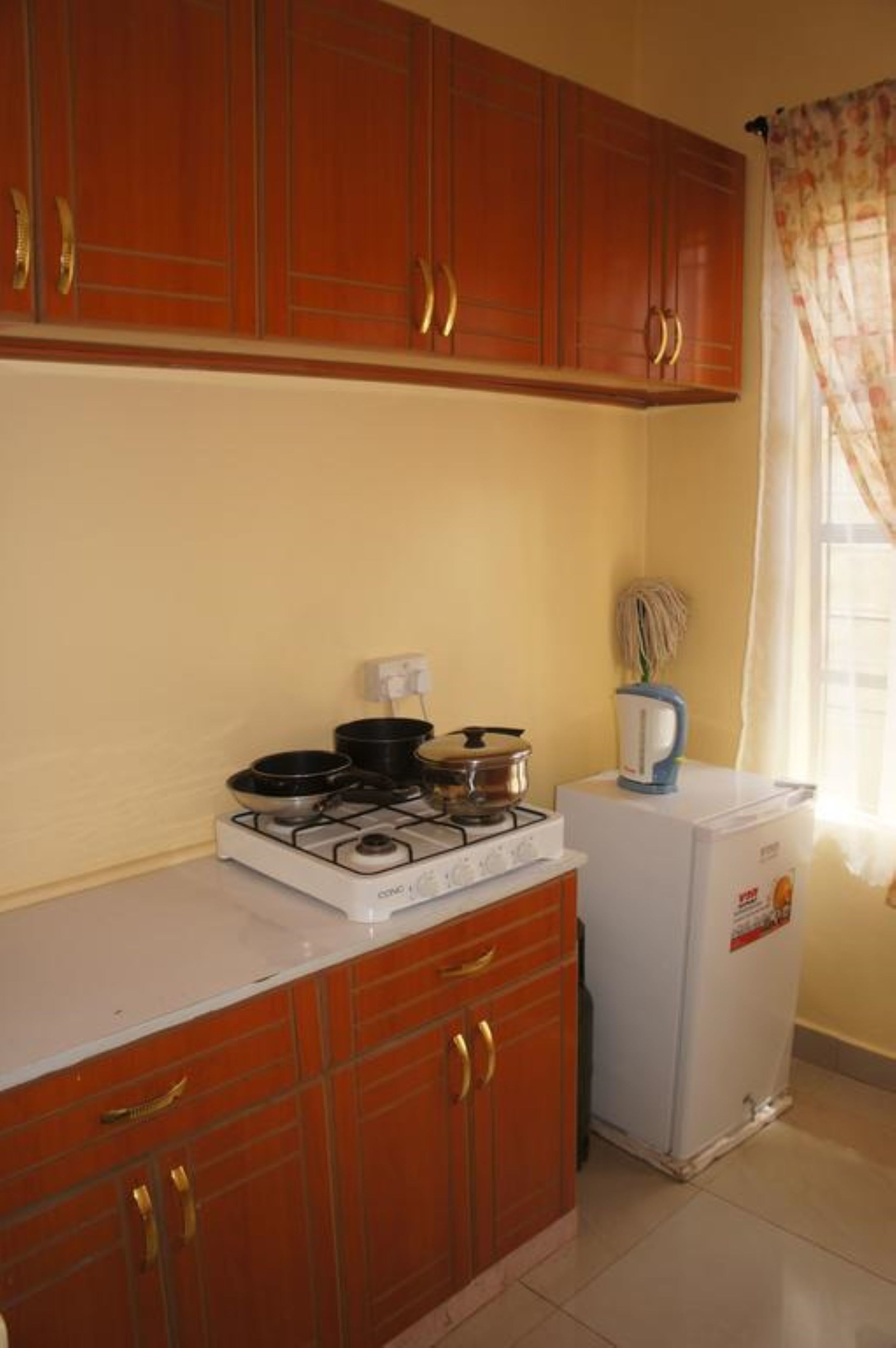 A compact kitchen with wooden cabinets, a gas stove, a kettle, and a small refrigerator.