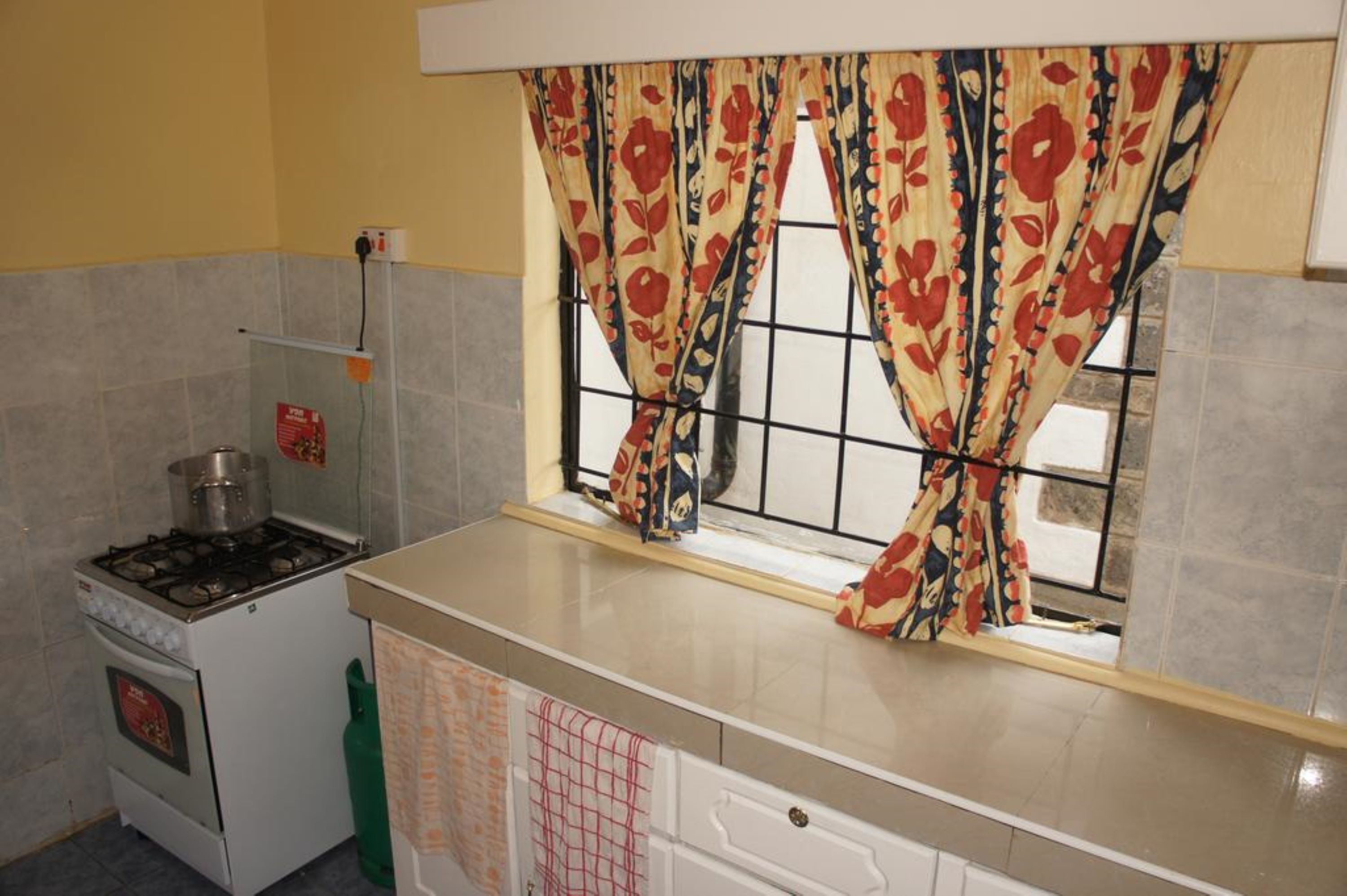 Une cuisine équipée d’une cuisinière à gaz, d’un petit four et d’une fenêtre agrémentée de rideaux à motifs floraux.