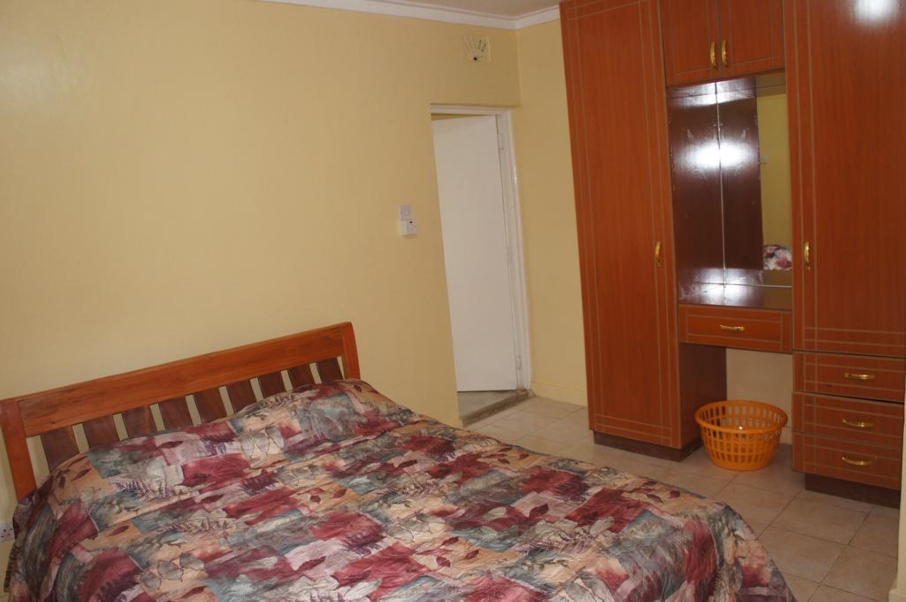 Una camera da letto con un letto, un armadio in legno e un piccolo cesto arancione.