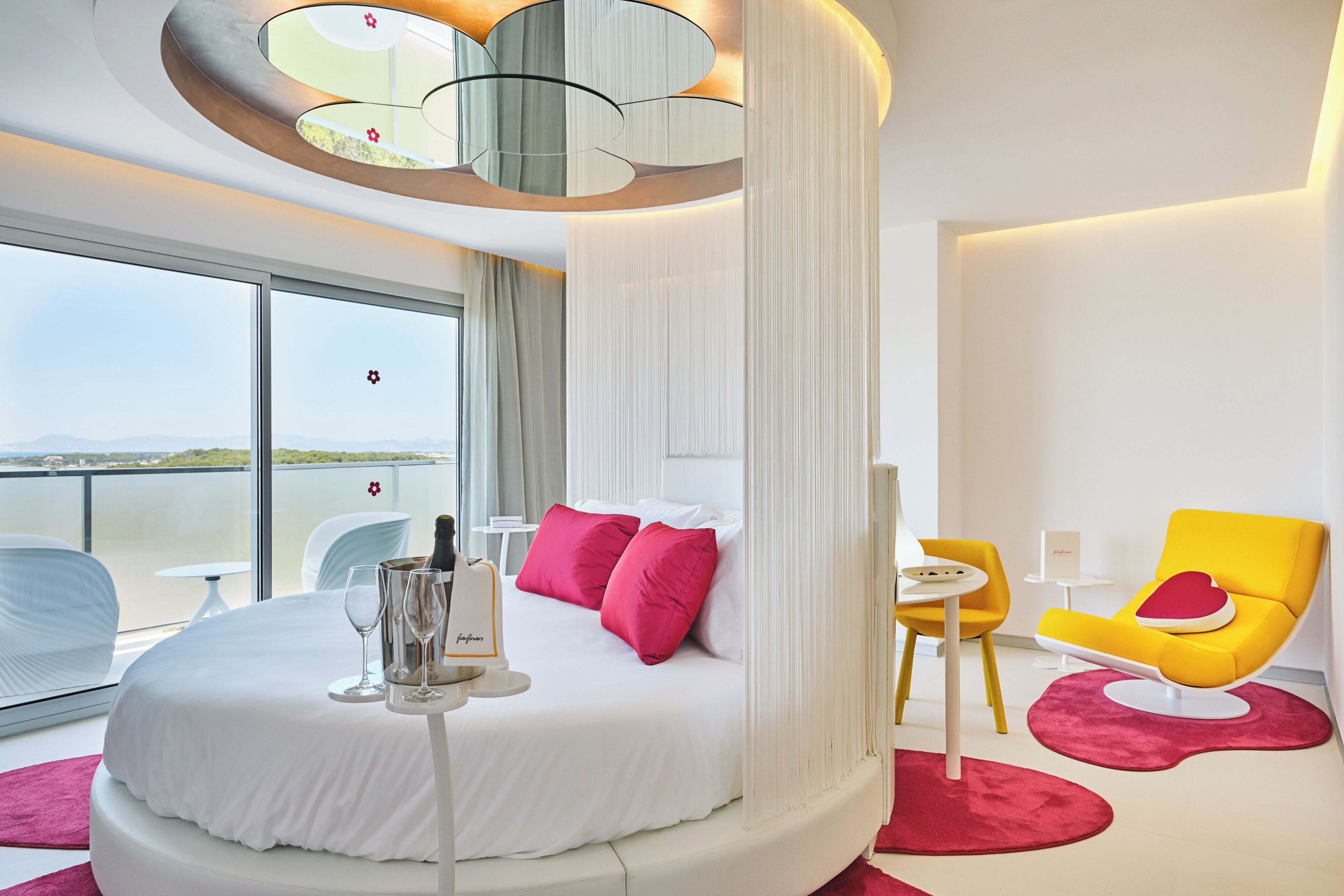 Una habitación de hotel moderna con una cama redonda, un balcón con vistas y una silla amarilla brillante.