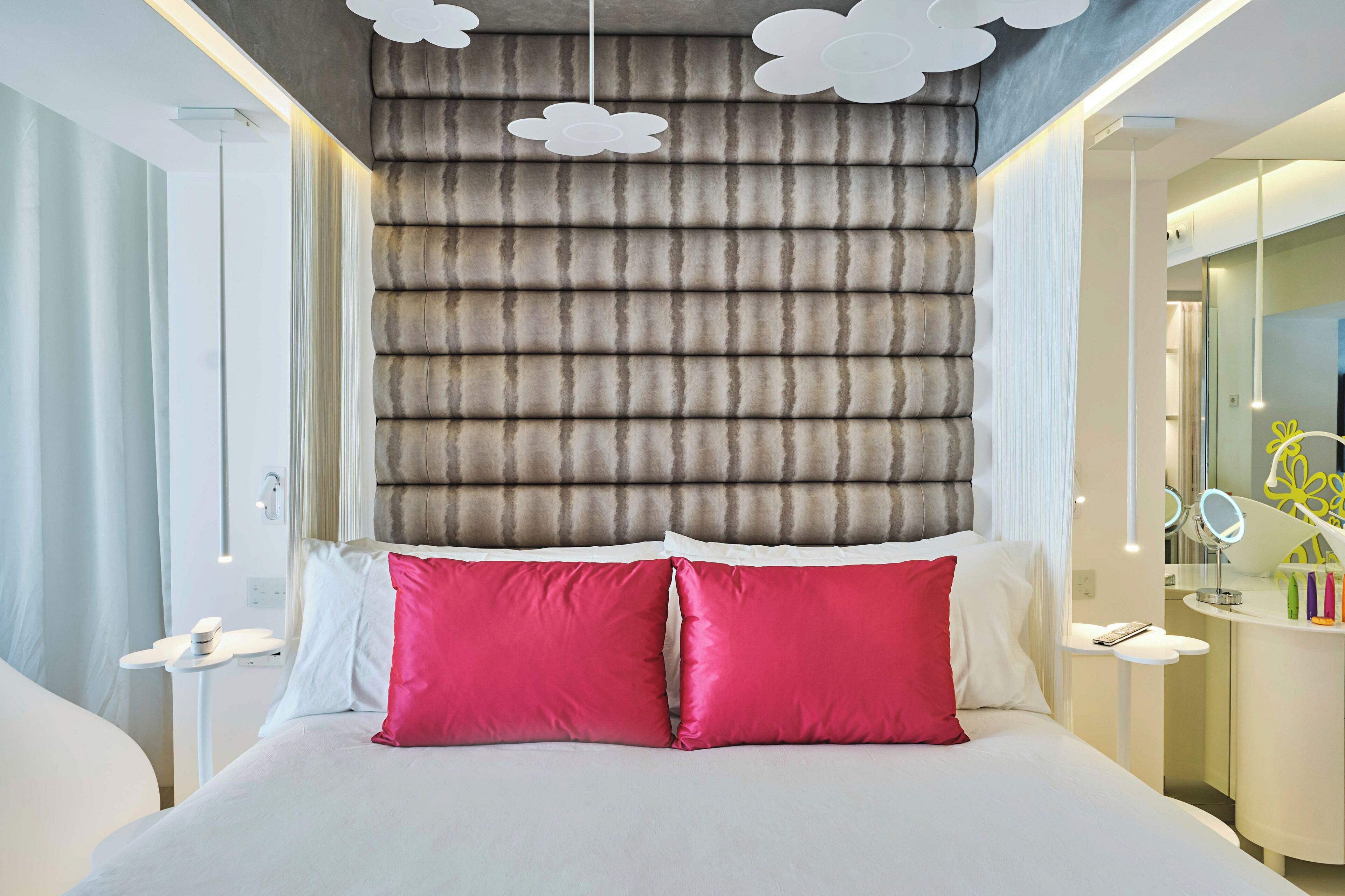 A modern hotel room with a large bed, a vanity with a mirror, and a wall with a textured pattern.