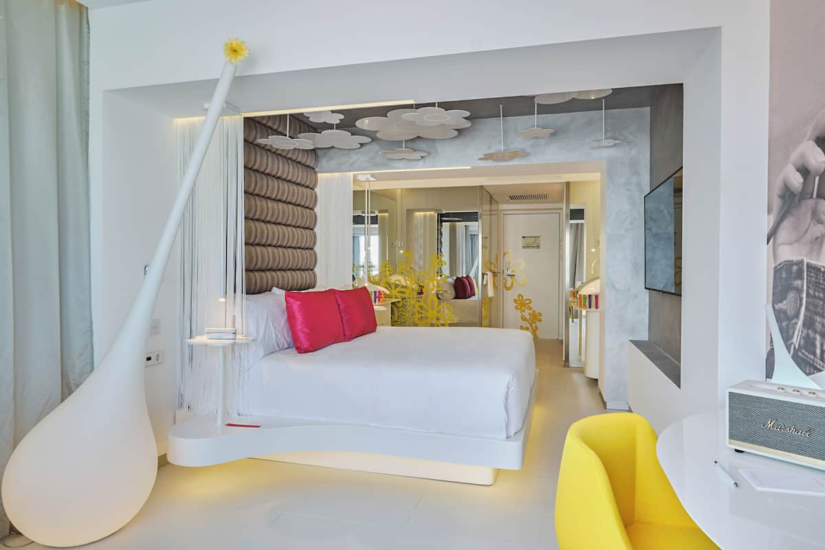 A modern bedroom with a large bed, a unique white vase, and a yellow chair.