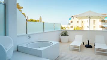 Un baño al aire libre moderno con una bañera, dos sillones blancos, una planta en maceta y una sombrilla grande.