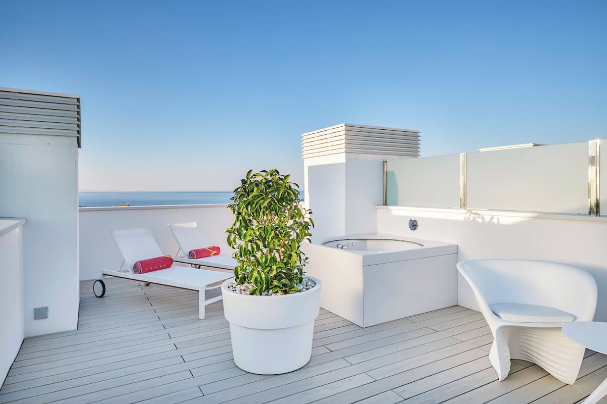 A rooftop terrace with a white lounge chair, a potted plant, a small sink, and a view of the sea.