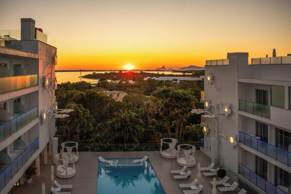 Una piscina en la azotea con sillones de descanso y vistas al atardecer.