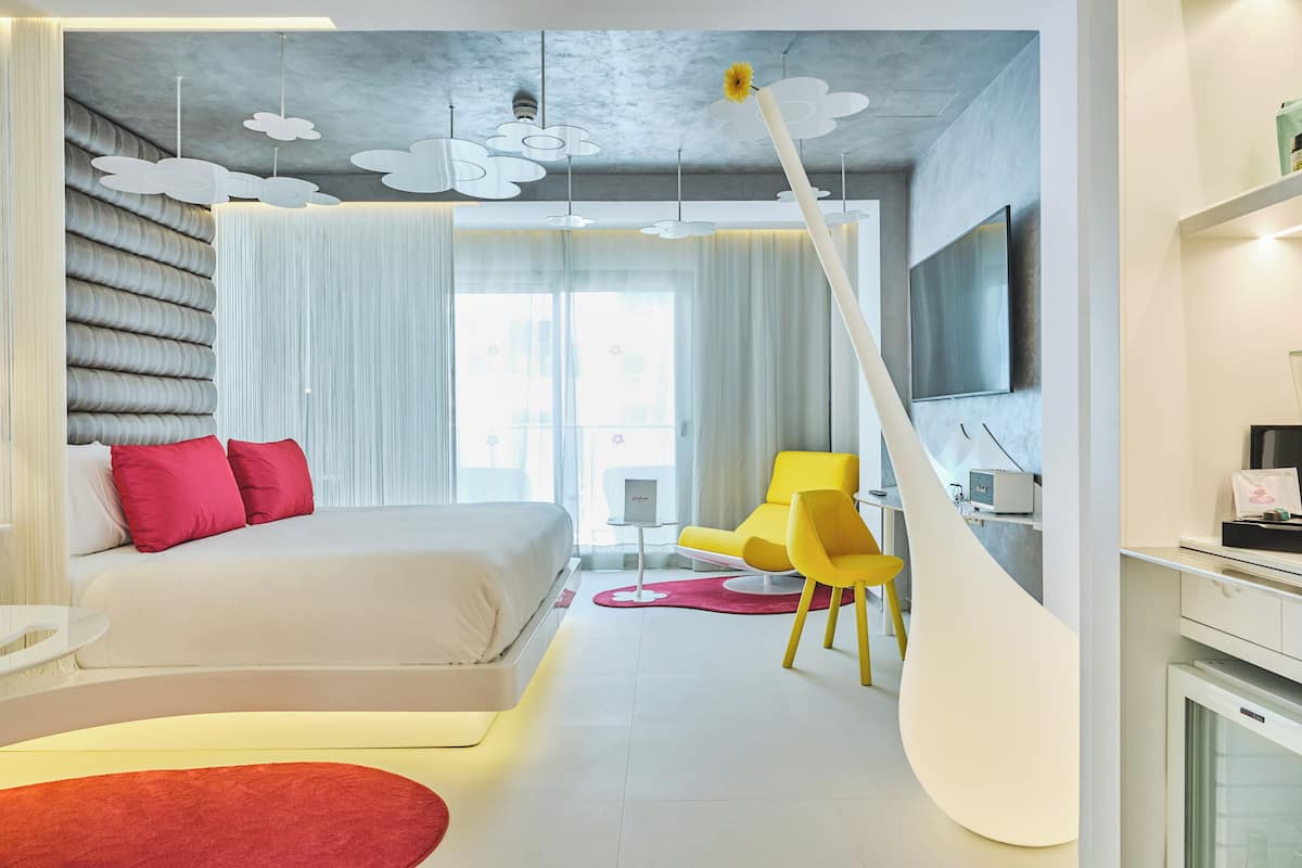 A modern hotel room with a bed, a desk, a chair, and a TV.