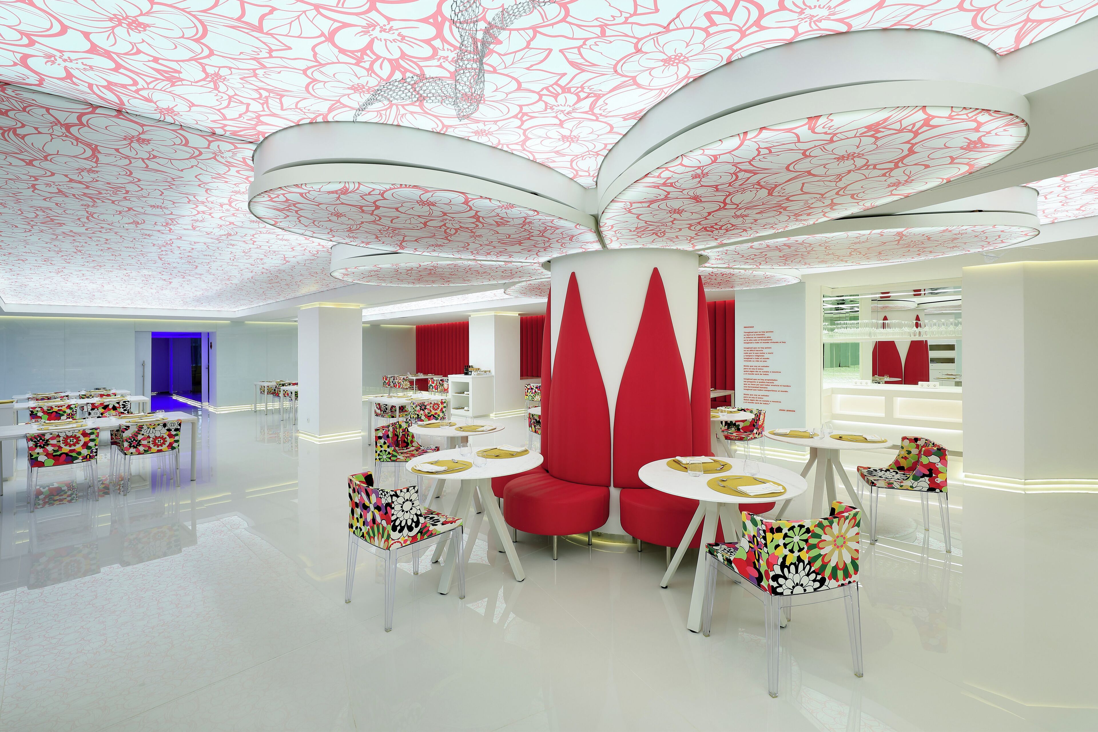 A modern interior with white and red furnishings, including round tables and chairs, and a ceiling with floral patterns.