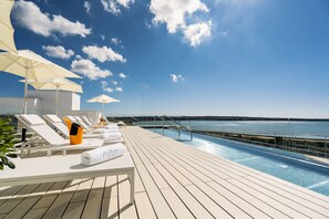 Zona junto a la piscina con tumbonas, sombrillas y vista al mar.