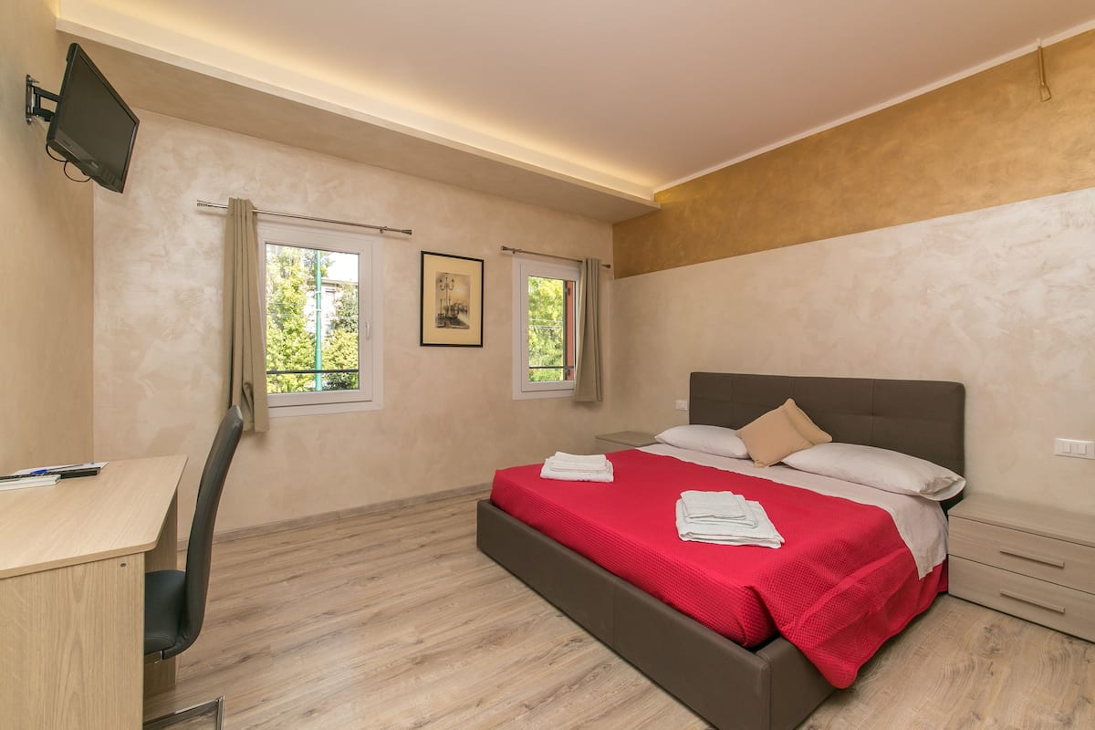 A bedroom with a bed, a desk, and two windows.
