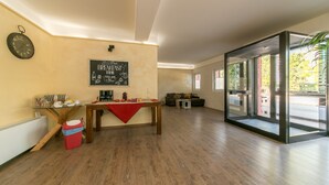 A spacious room with a wooden floor, a breakfast sign on the wall, a coffee machine, and a glass door leading outside. - Red Lion Guest House (Mestre)